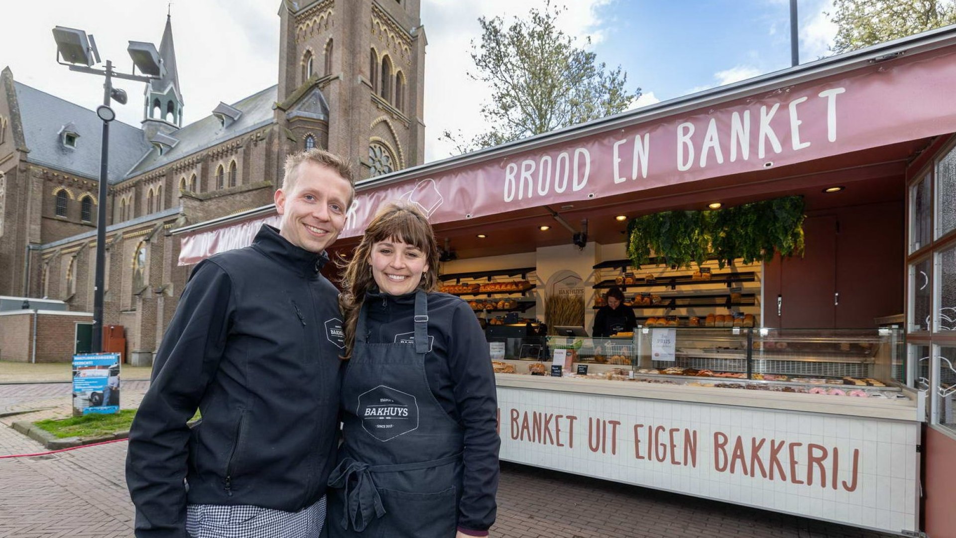Lachende eigenaar en eigenaresse staan vóór hun verkoopwagen voor brood en banket